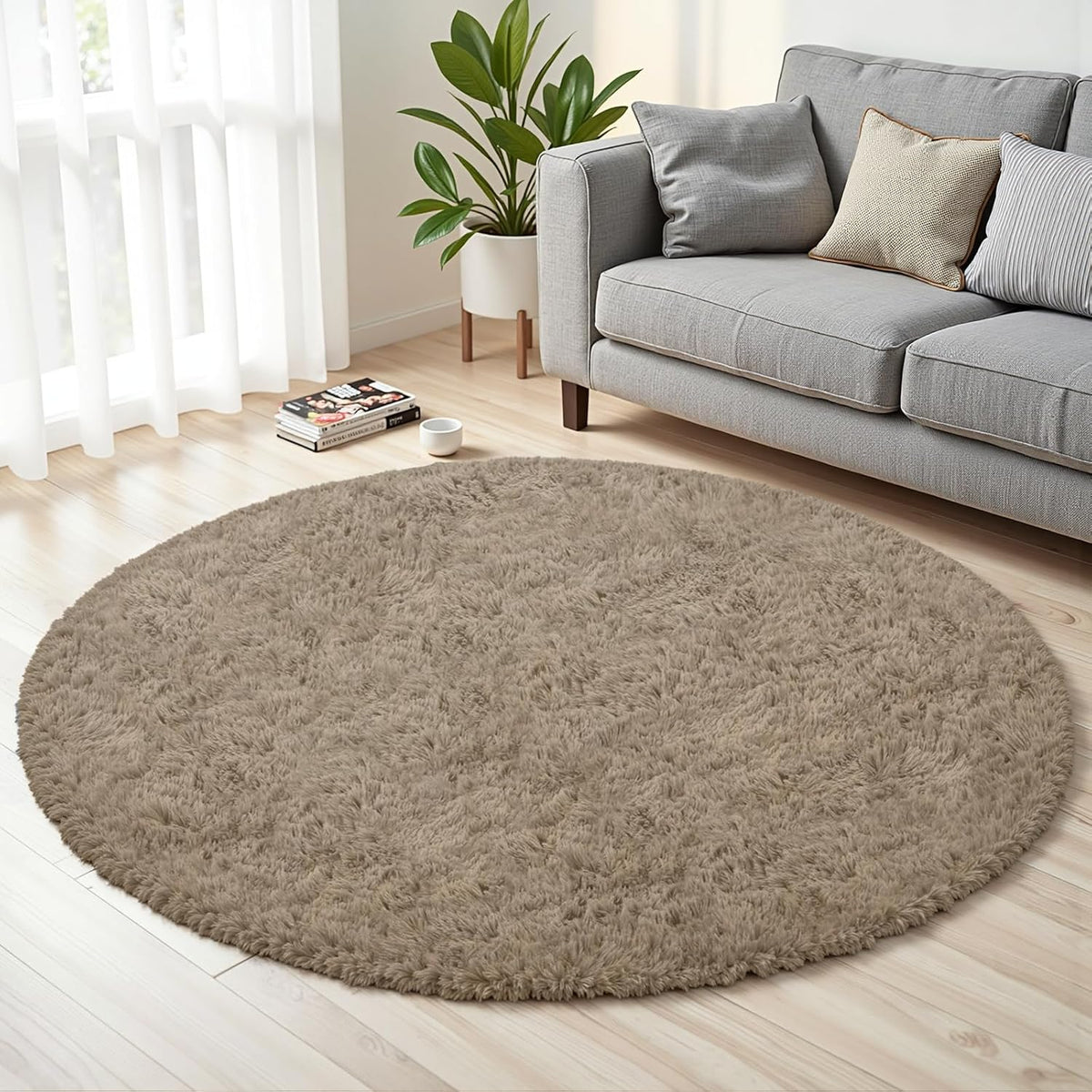 Round taupe shag rug on light wood floor beside a gray sofa and potted plant