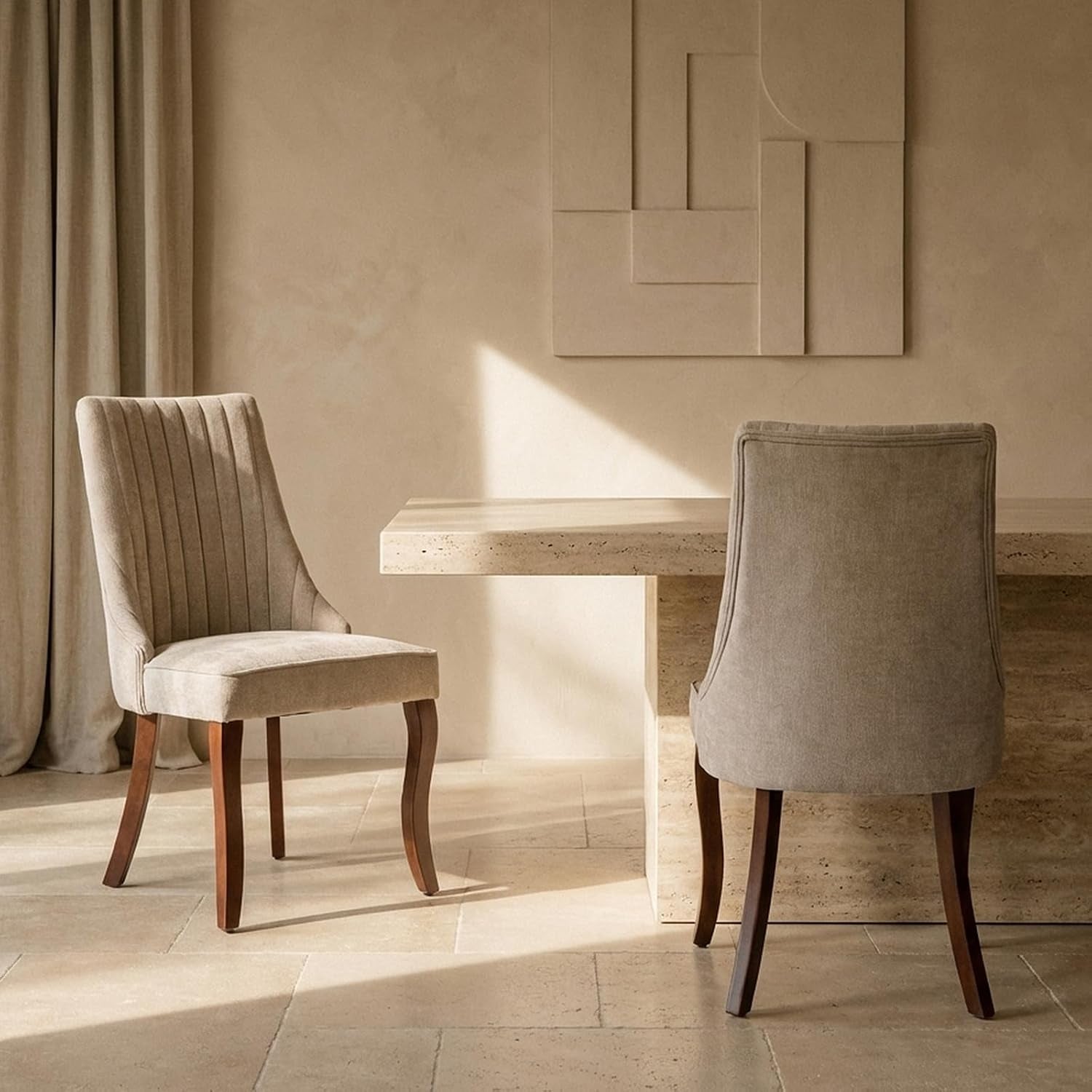 Two beige upholstered dining chairs with curved dark wooden legs beside a stone dining table.