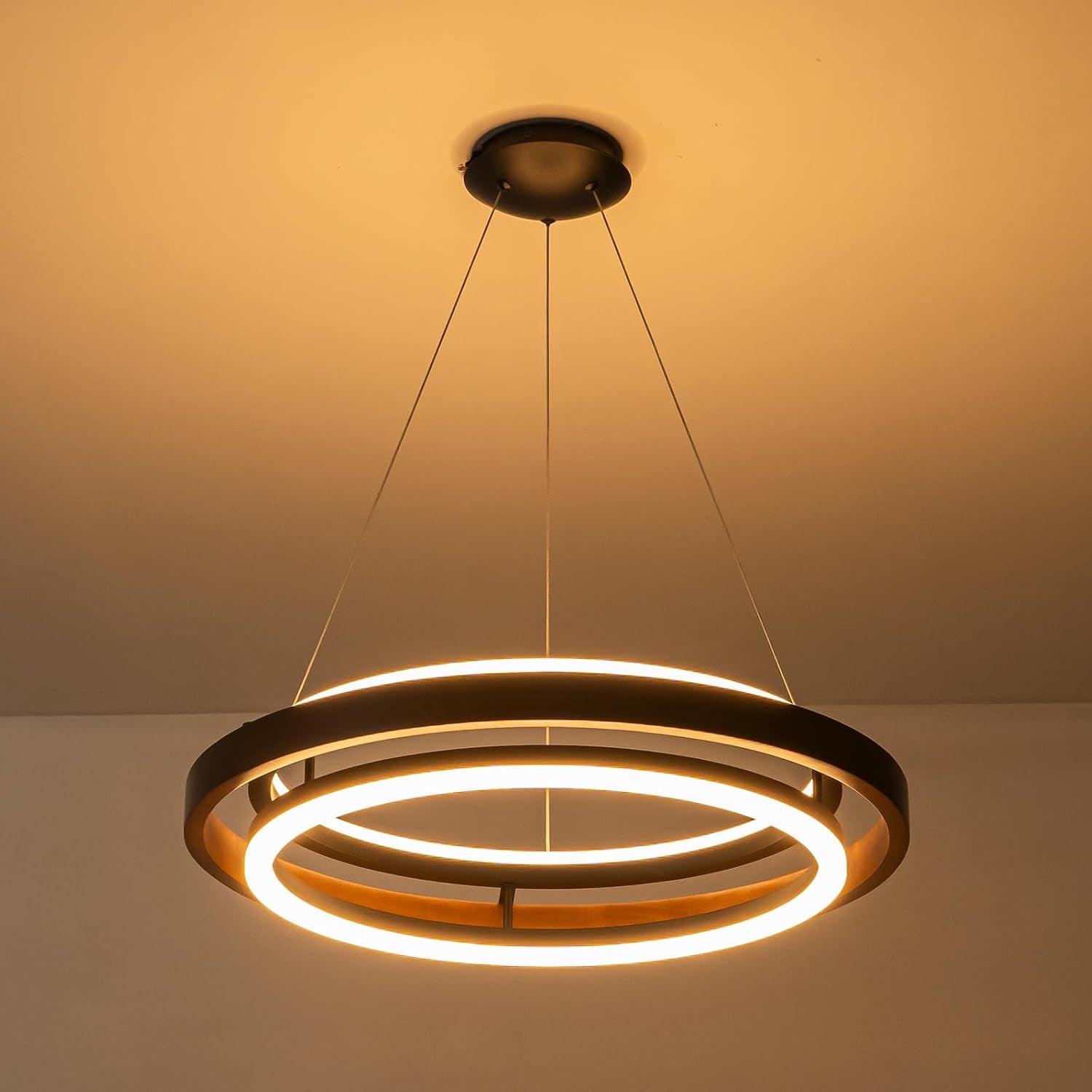 Close-up underside view of a two-ring wood pendant light glowing warmly from thin suspension cables.