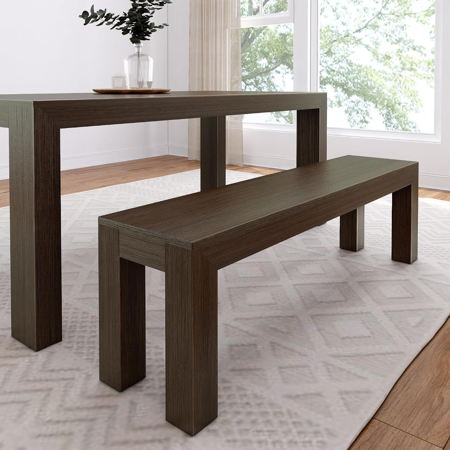Side perspective of a table and bench set in a warm dark brown wood finish on a light rug