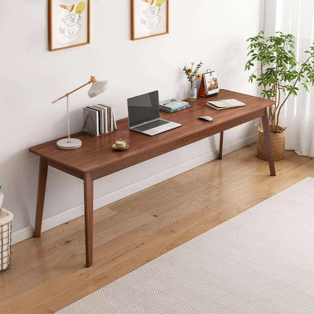 Side view of a walnut long desk against a white wall styled with a lamp, laptop, books and a potted plant in a basket.