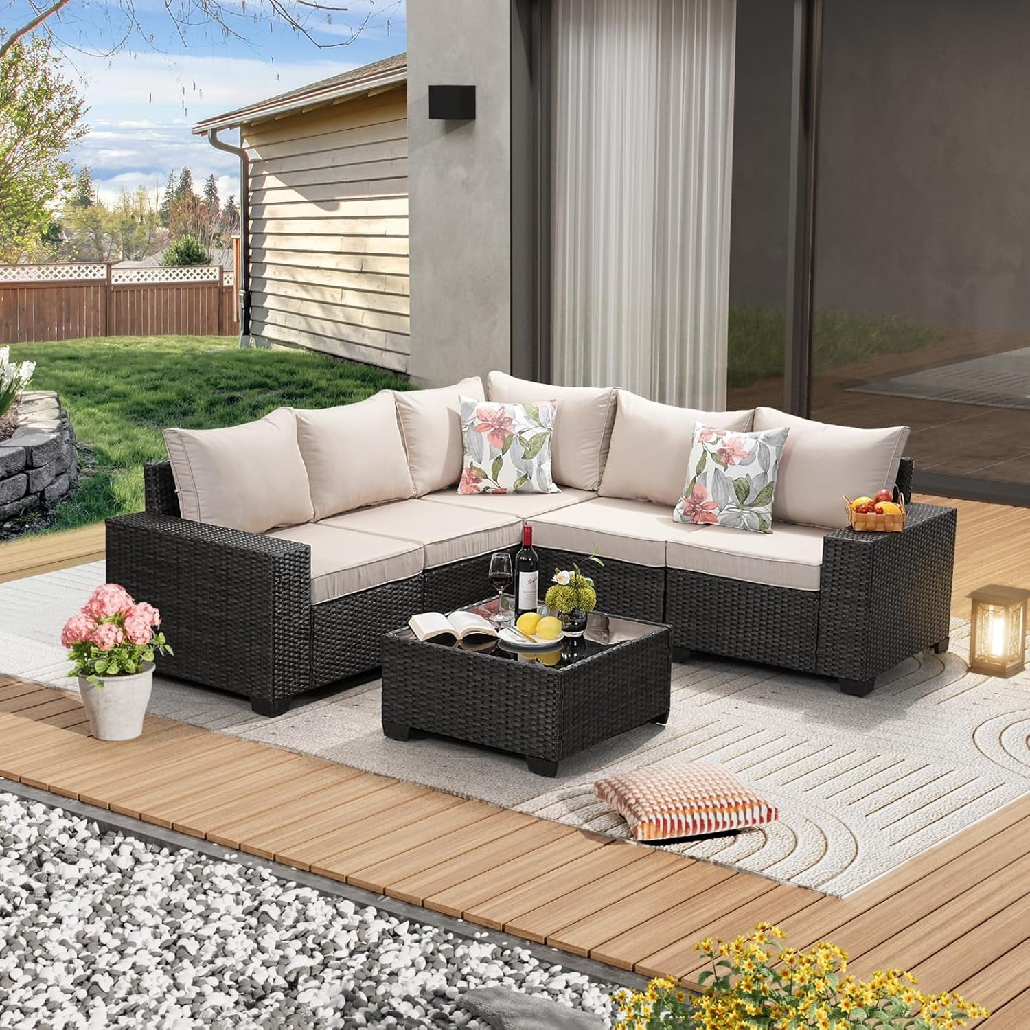 Close angled view of the L-shaped rattan sofa with beige cushions and a glass-top coffee table on a rug near a sliding glass