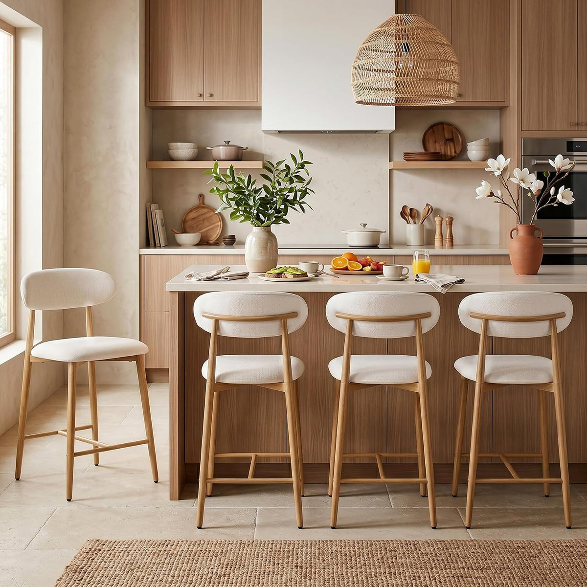 Three light beige upholstered counter stools at an island in a bright kitchen with a single stool to the left.