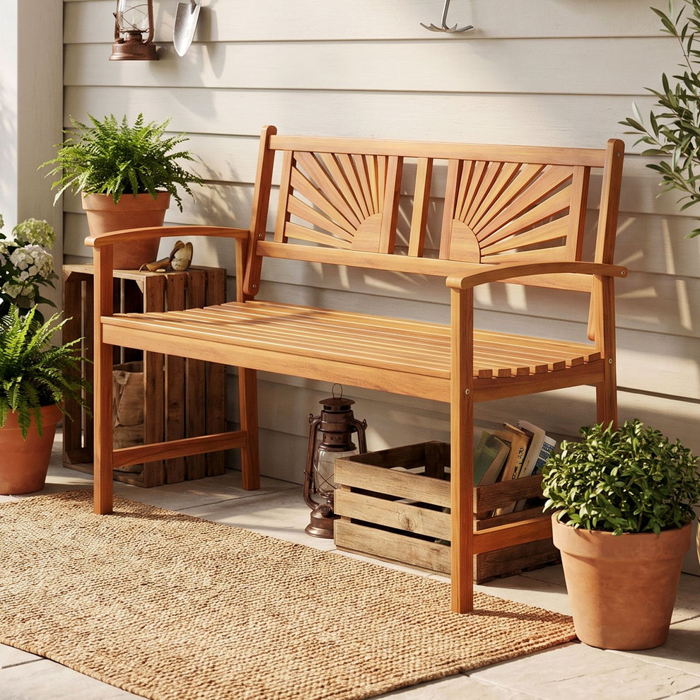 Wooden garden bench with sunburst back and curved arms on a porch, surrounded by potted plants.
