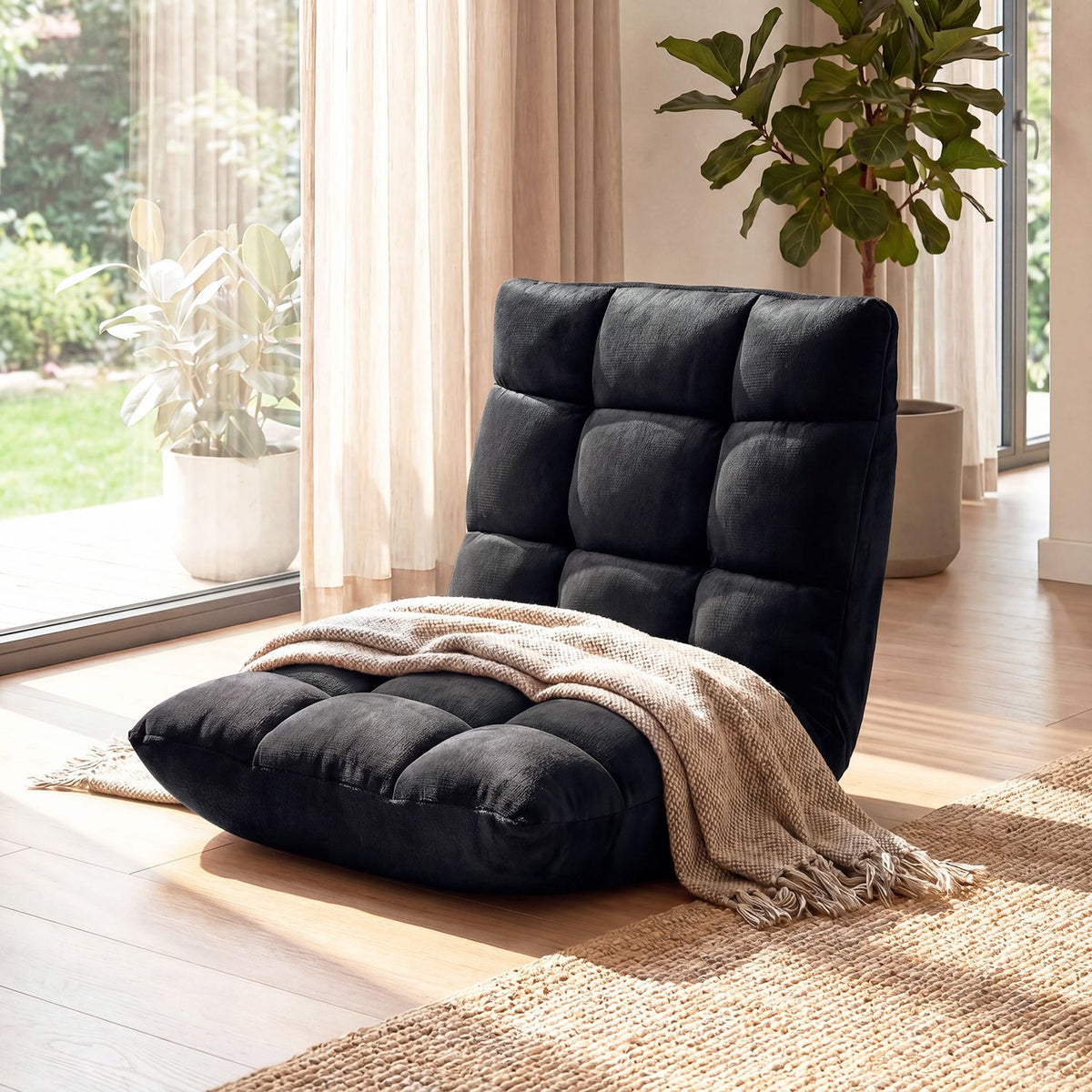 Black cushioned floor chair with a beige throw in a bright room by large windows.