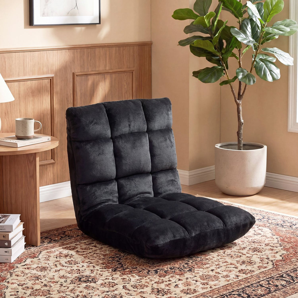 Black tufted floor chair sits on a patterned rug beside a wooden side table and potted plant.