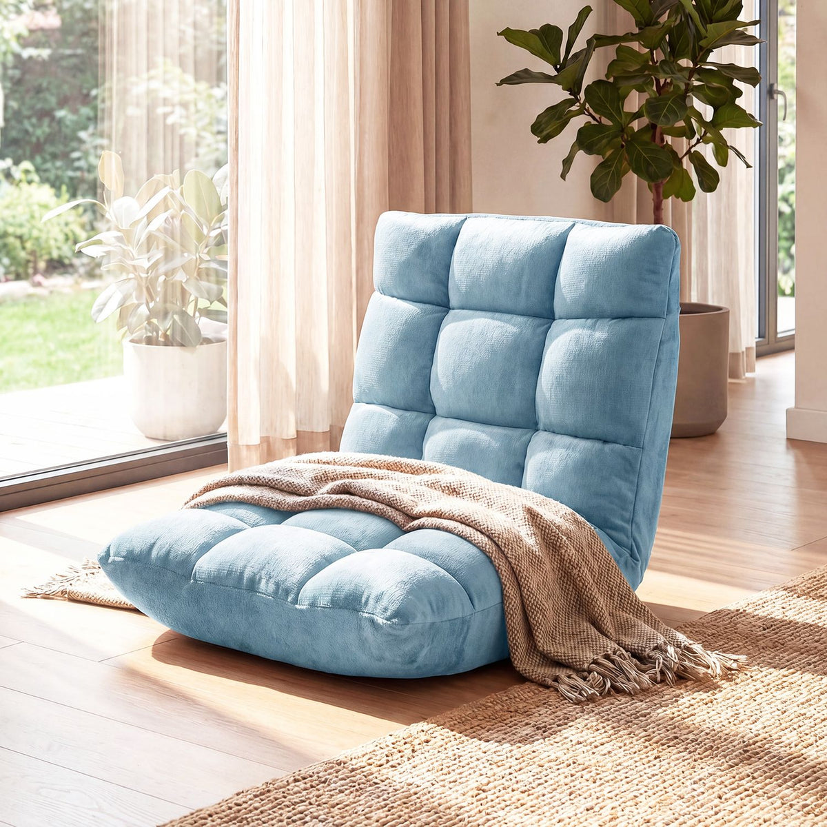 Blue tufted floor chair with a draped throw on a rug beside bright windows and potted plants.