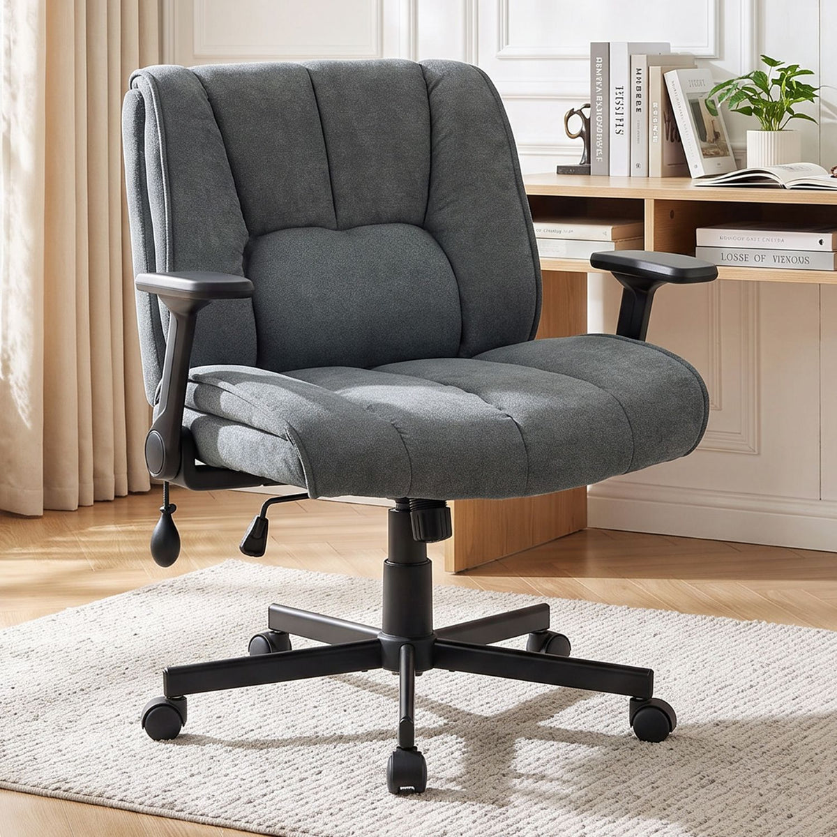 Charcoal upholstered office chair with padded arms and five-wheel base beside a desk in a bright room.