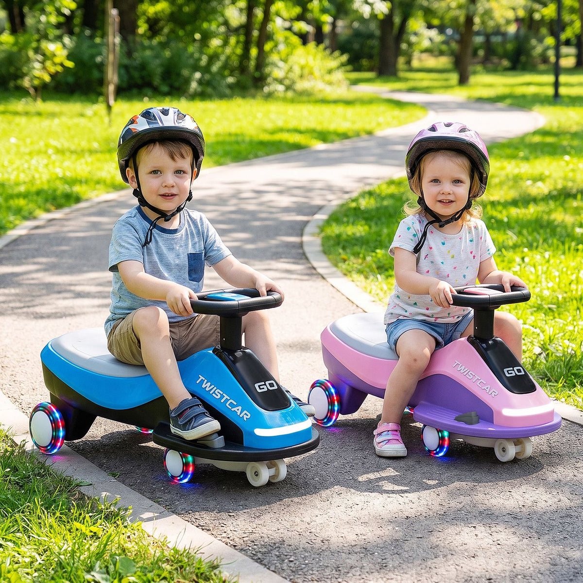 Two children wearing helmets sit on blue-and-black and pink-and-purple ride-on cars on a park path.