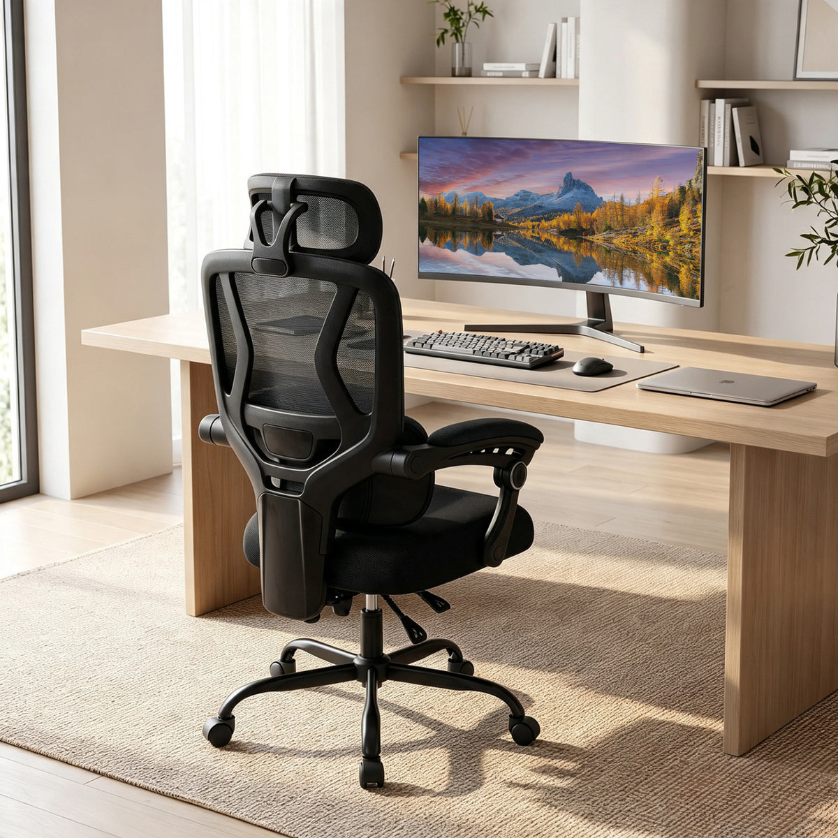 Black mesh office chair viewed from behind at a wooden desk in a bright home office.
