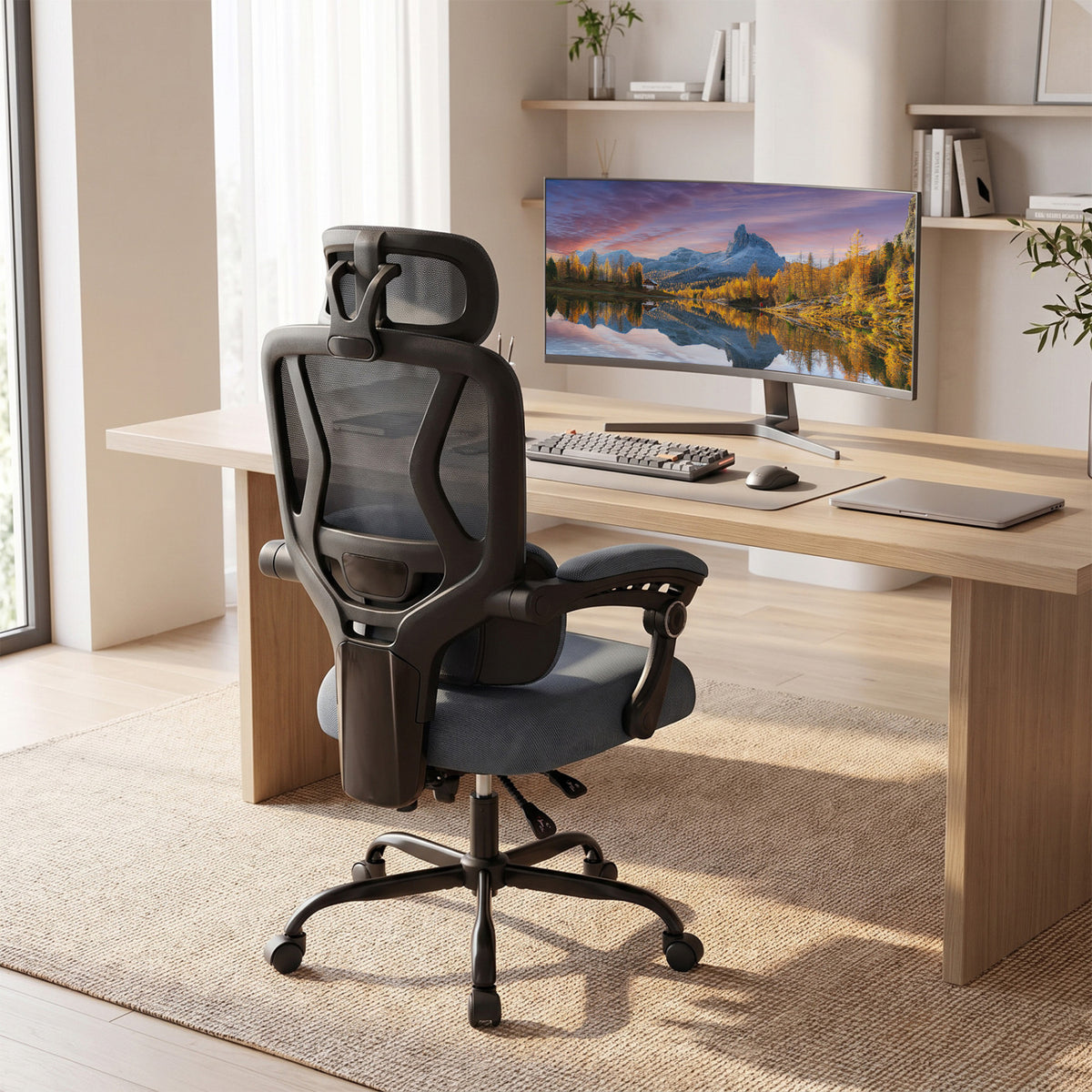 Black mesh office chair viewed from behind at a desk in a bright home office.