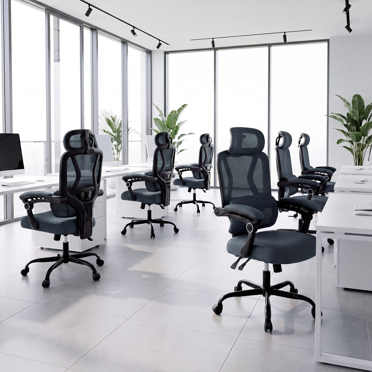 Several dark mesh office chairs arranged around desks in a bright, window-lined office.