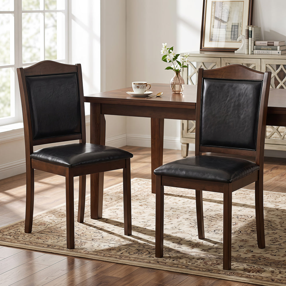 Two dark upholstered wooden dining chairs beside a dining table in a bright room.