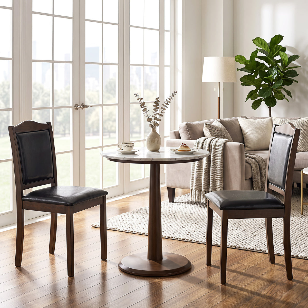 Two dark upholstered wooden chairs arranged around a pedestal table near a sofa and large windows.