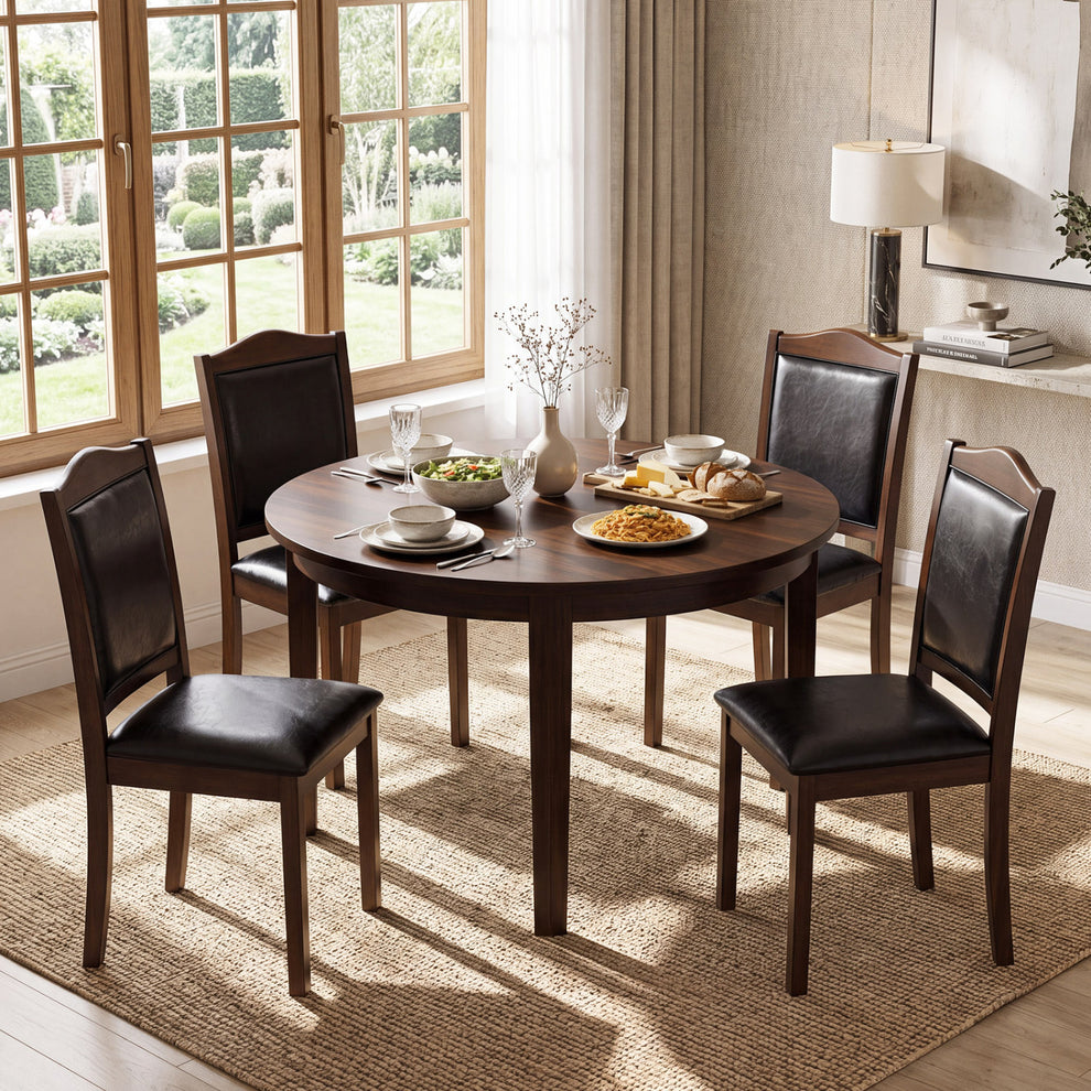 Four dark upholstered wooden chairs surround a round dining table beside large windows.
