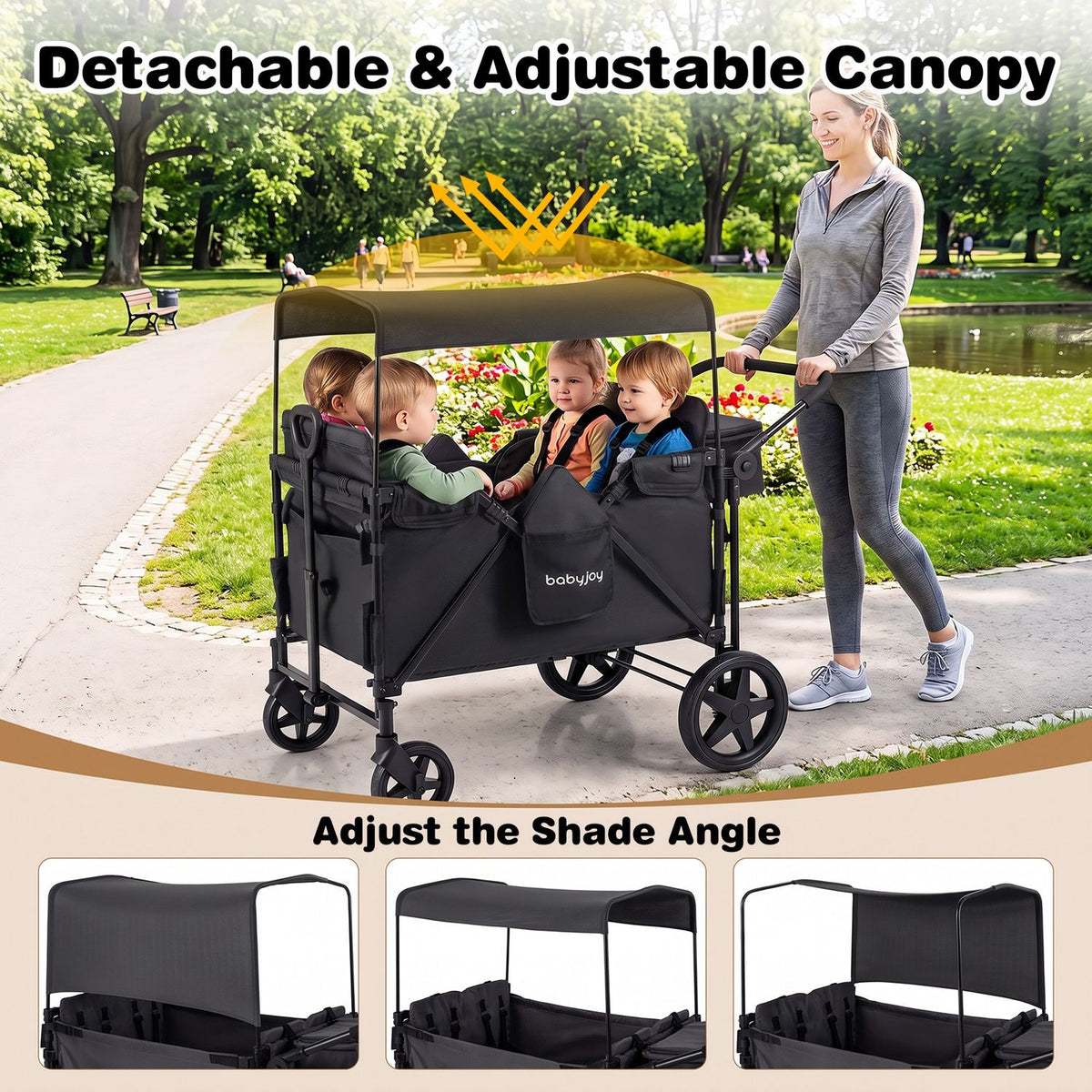 A woman pushes a black covered wagon with three children seated inside along a park path.