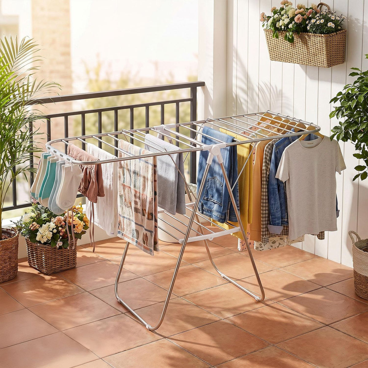 Silver folding clothes rack filled with laundry on a tiled patio beside a white wall