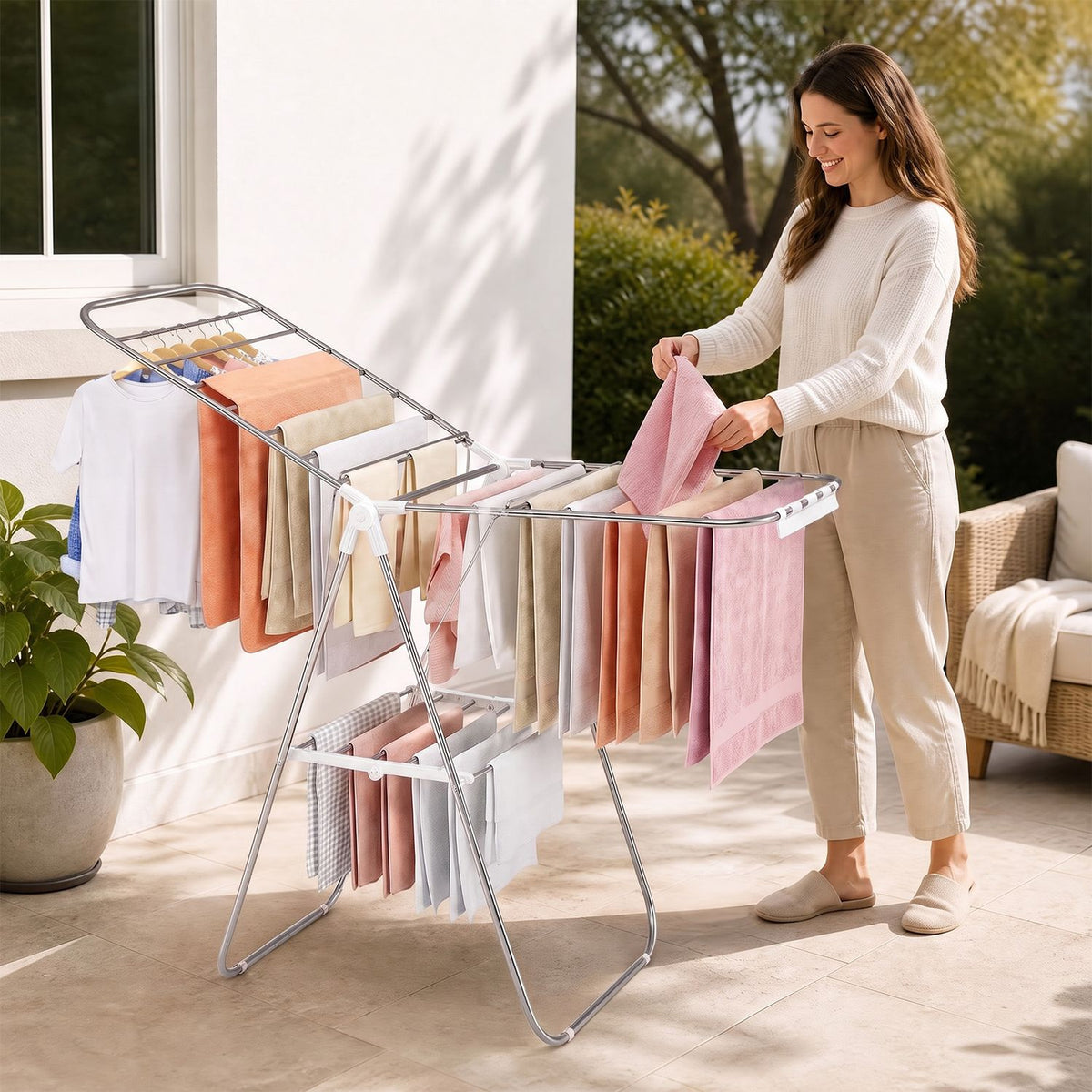 Woman hanging a pink towel on a silver drying rack in a sunny outdoor setting