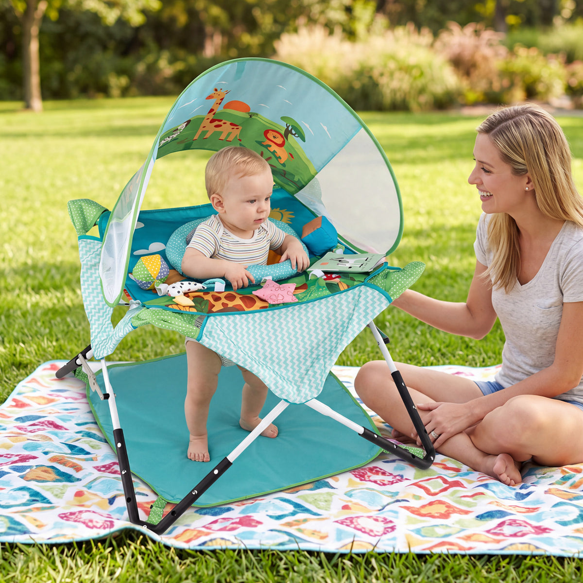 A baby plays beneath a printed canopy in a portable jumper on the grass beside an adult.