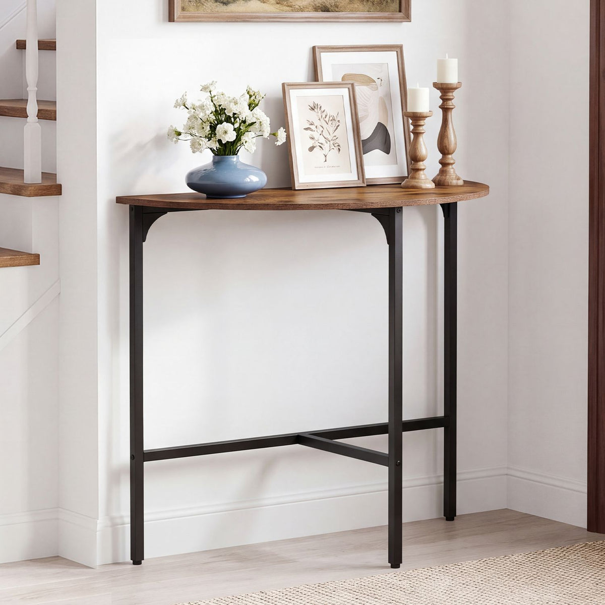 Half-moon console table with a rustic brown top and black metal frame, styled with flowers, framed art, and candleholders.