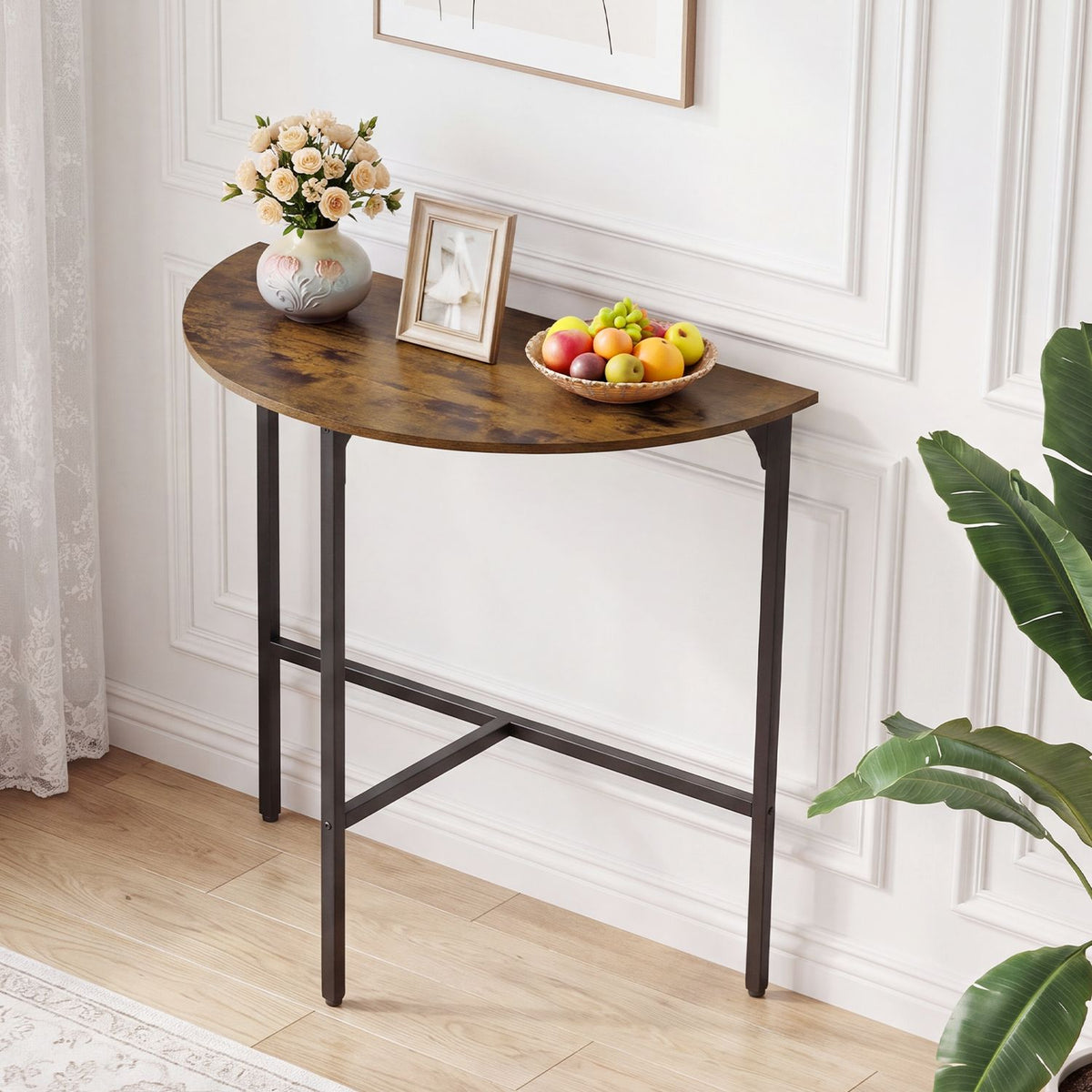 Angled view of a half-moon console table against a paneled wall, topped with flowers, a photo frame, and fruit.