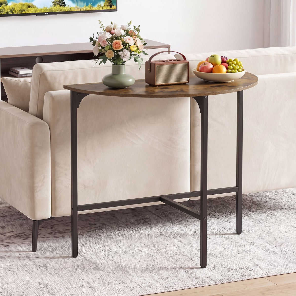 Rustic brown half-moon console table with dark metal frame behind a cream sofa, decorated with flowers, a radio and fruit.