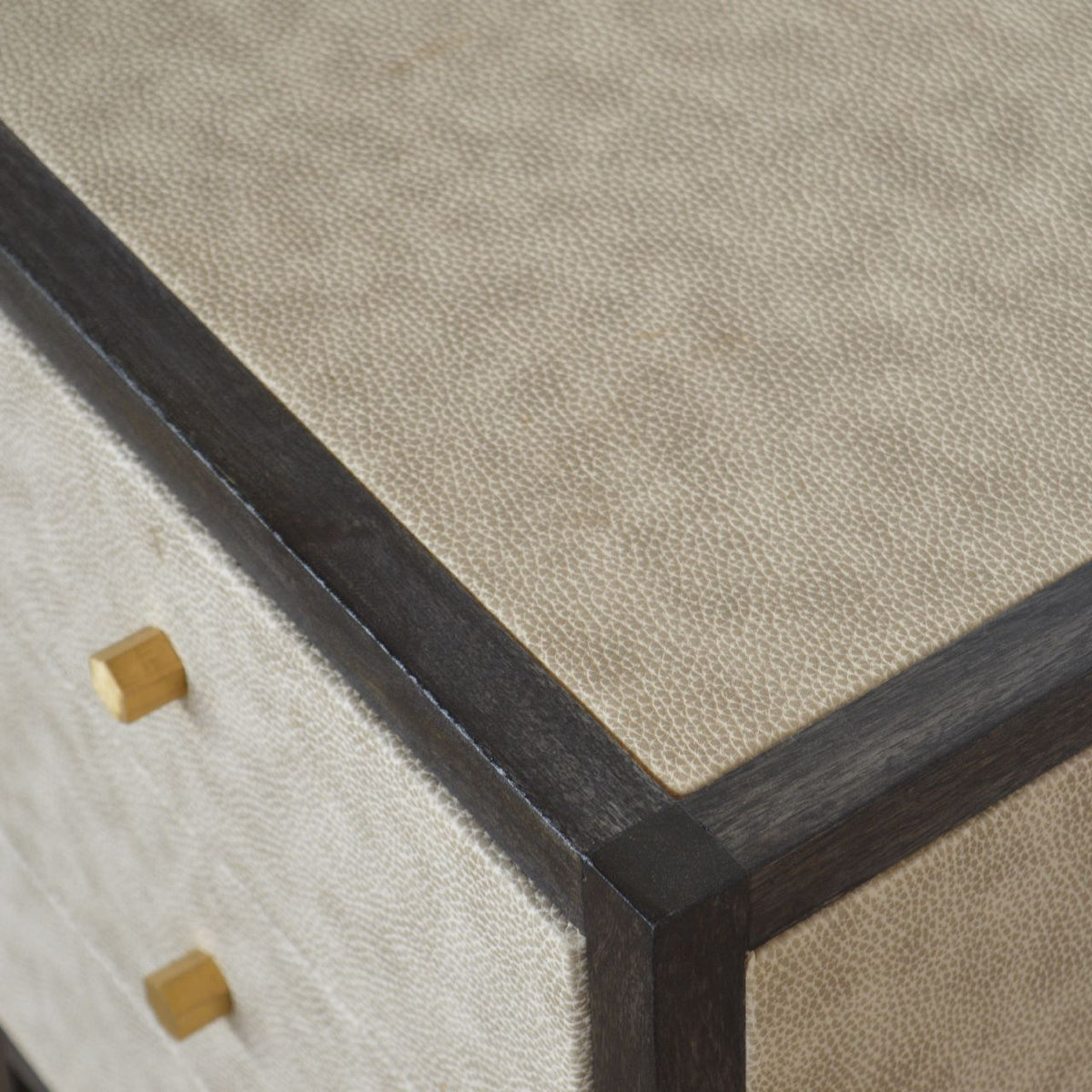 Close-up of textured faux leather, dark frame and gold-tone drawer knobs