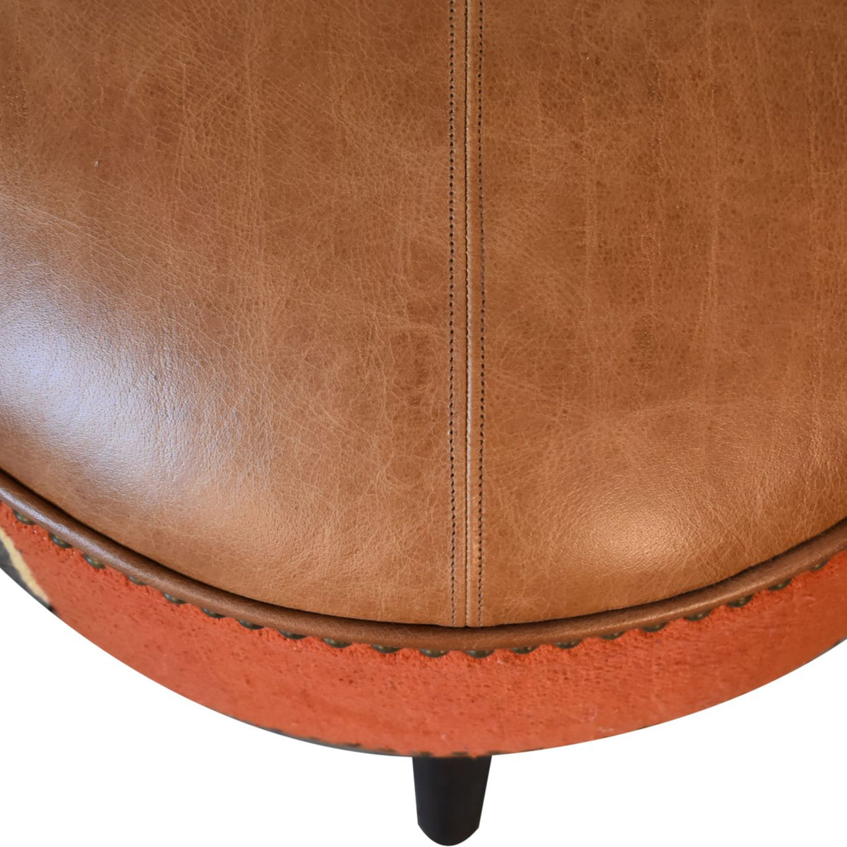 Close-up of the tan leather top and rust fabric side of the round footstool.