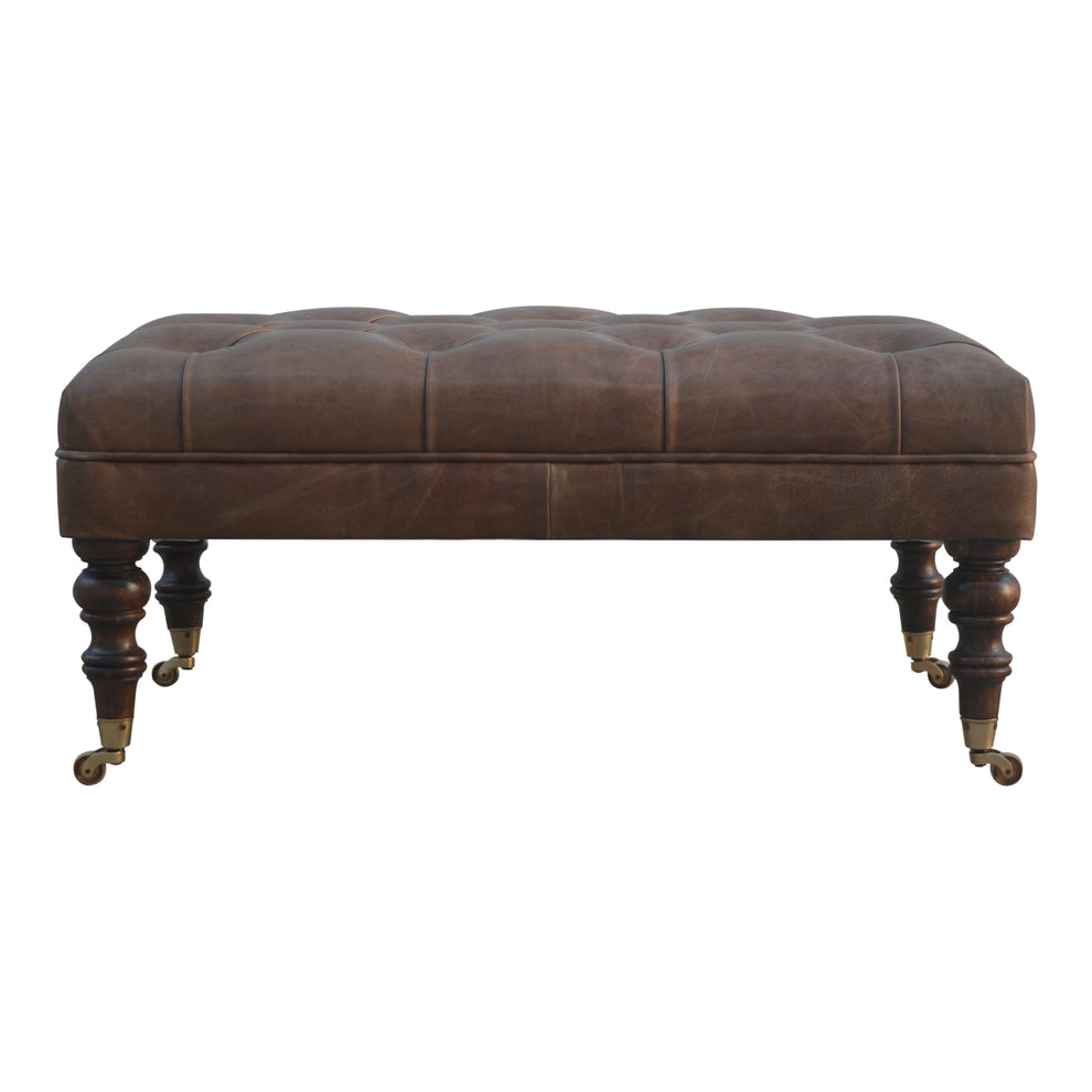 Brown leather ottoman in straight-on front view with buttoned top and turned legs.