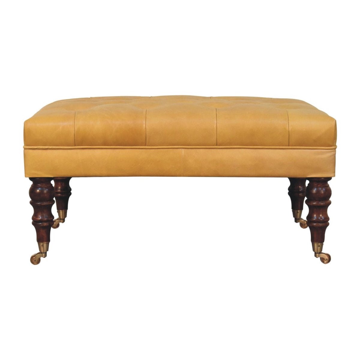 Straight-on view of a tan ottoman with stitched leather panels and carved dark legs with casters.