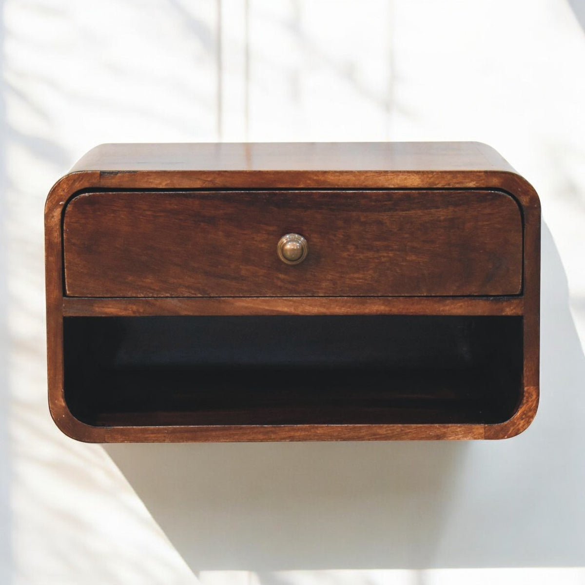 Curved walnut bedside table with a small round drawer pull above an open shelf.