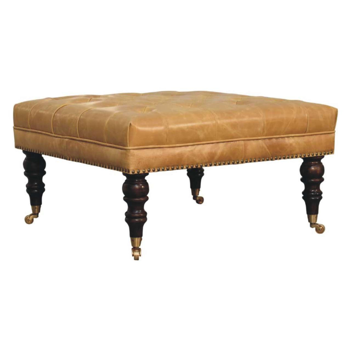 Tan ottoman viewed from the front corner, showing its cushioned top and four dark turned legs with casters.