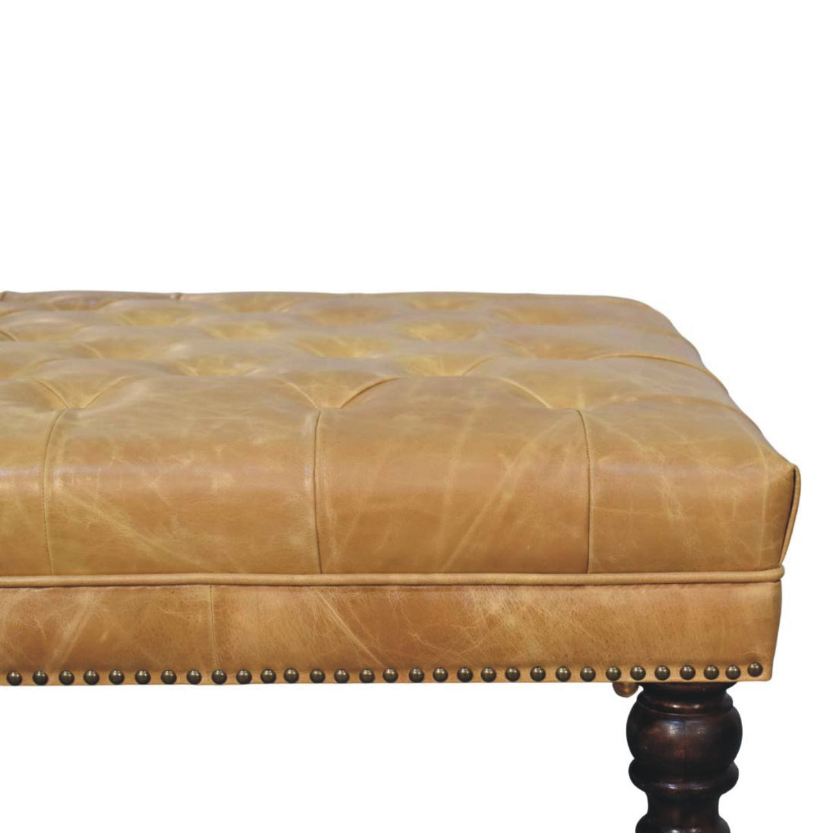 Close-up of the tan cushioned top, stitched seams, nailhead trim, and one dark turned leg.