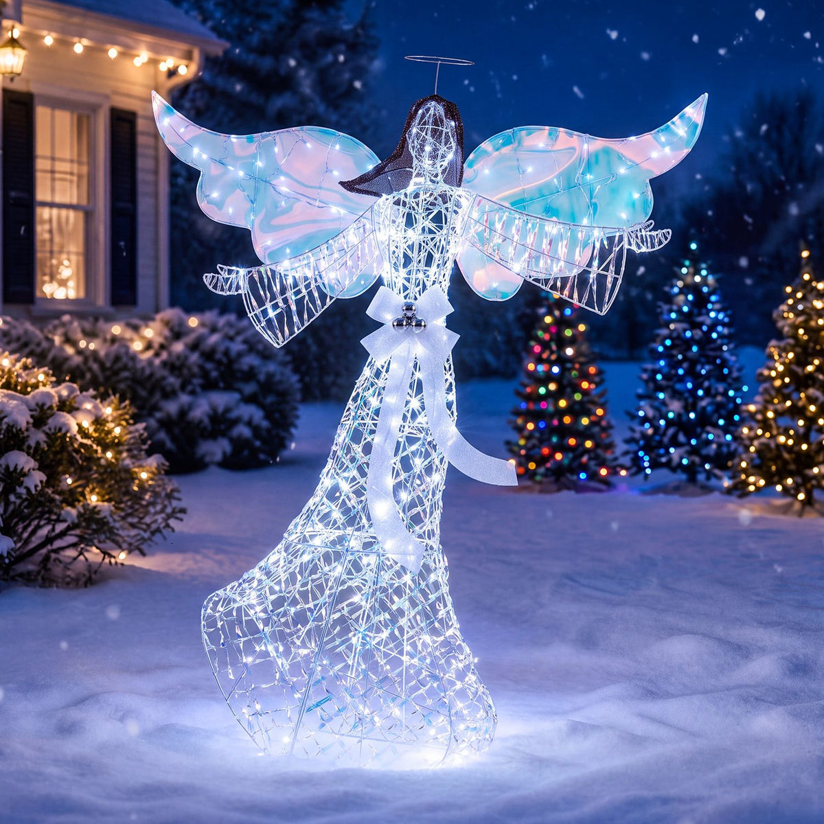 A glowing iridescent angel stands in snow at night, with lit Christmas trees and a house behind it.