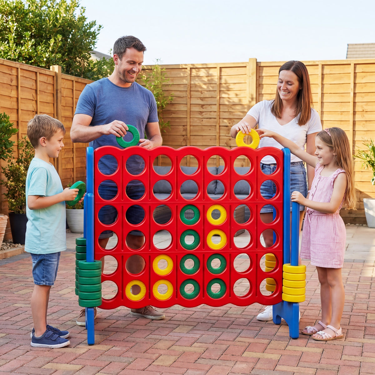 A family plays at the oversized game board on a patio, with colored discs and side storage stacks visible.