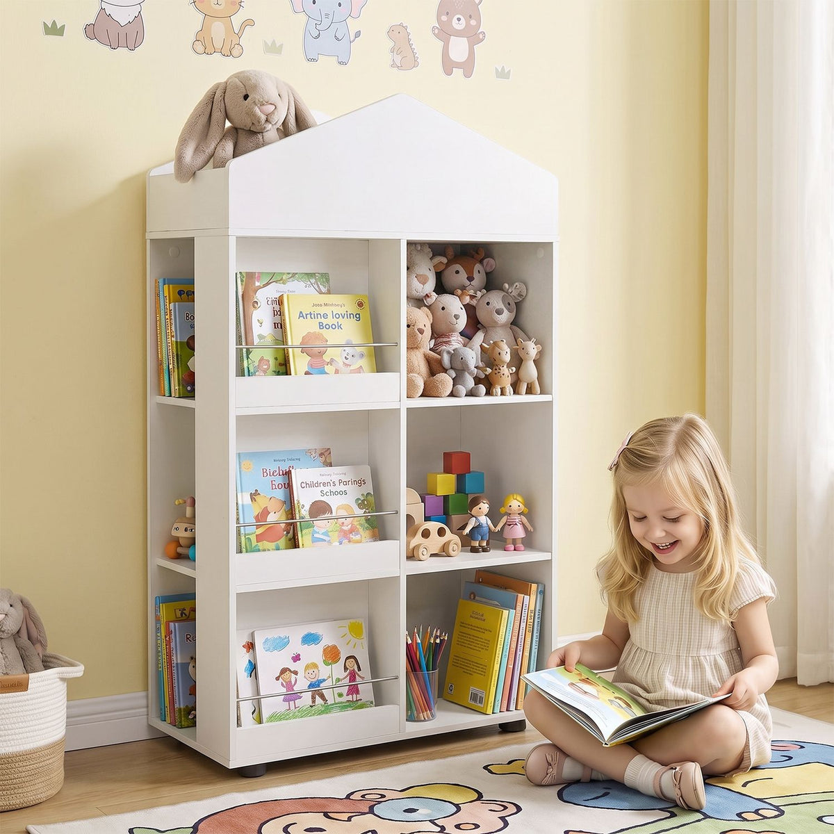 A girl reads beside a white house-shaped bookshelf holding books, stuffed animals, toys, and art supplies.