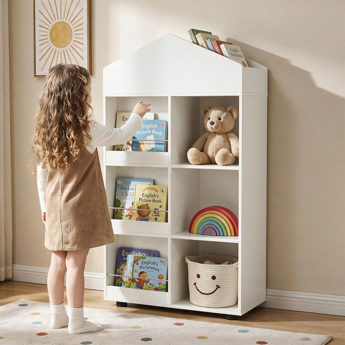 A child reaches for a book on a white house-shaped bookshelf filled with books, a teddy bear, a basket, and toys.
