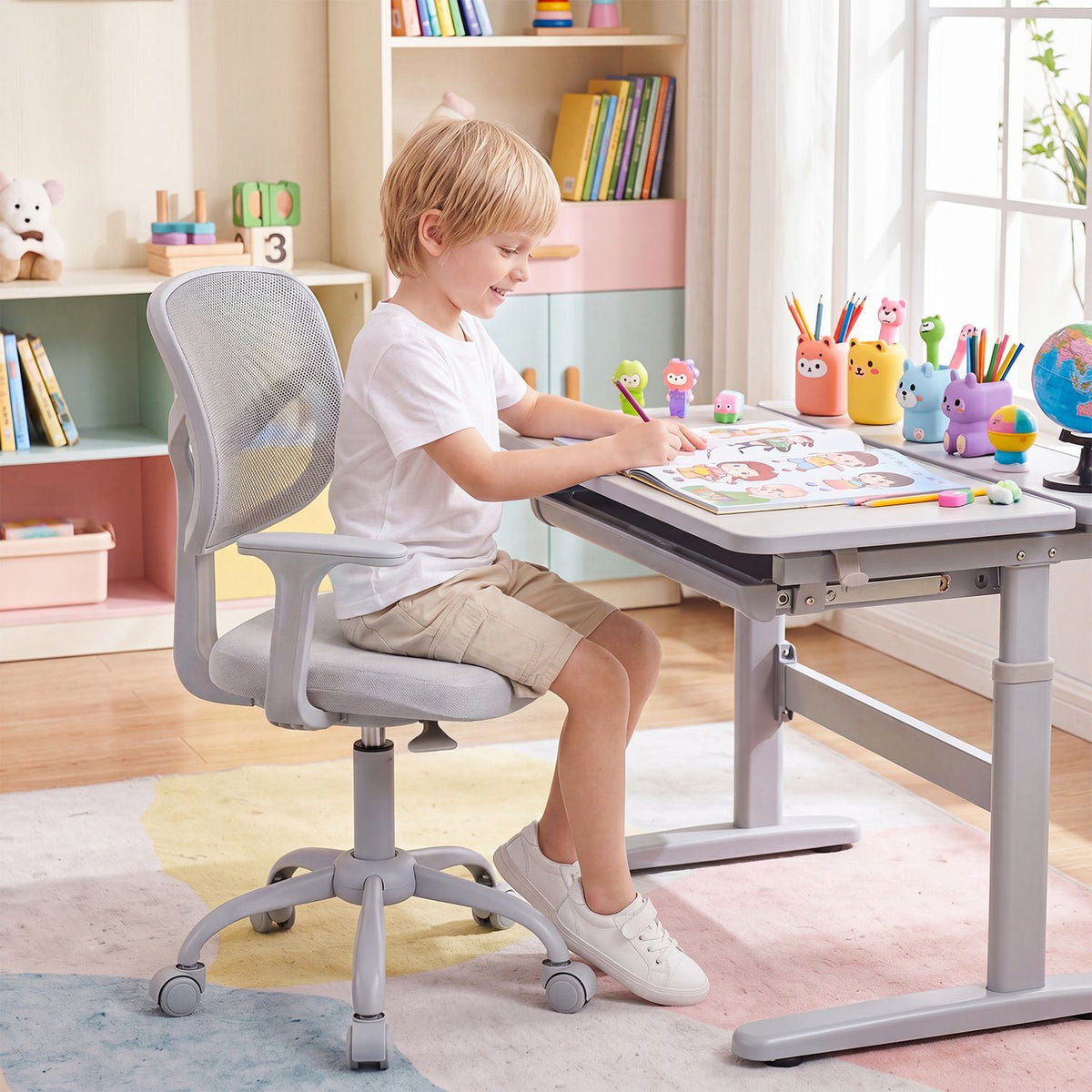 A child sits in a gray mesh-back chair at a desk, drawing in a bright study room.
