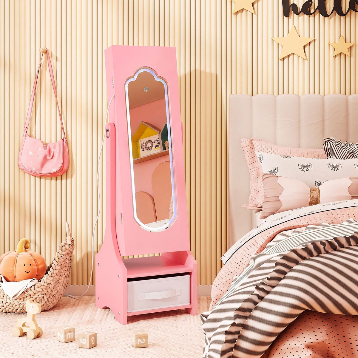 Pink standing jewelry armoire with a full-length mirror beside a bed in a softly decorated bedroom.