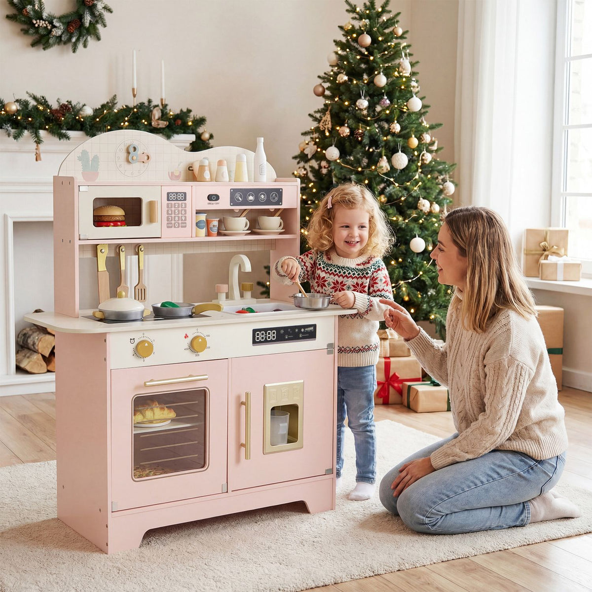 A child plays at the pink toy kitchen while an adult kneels beside her in a decorated living room.