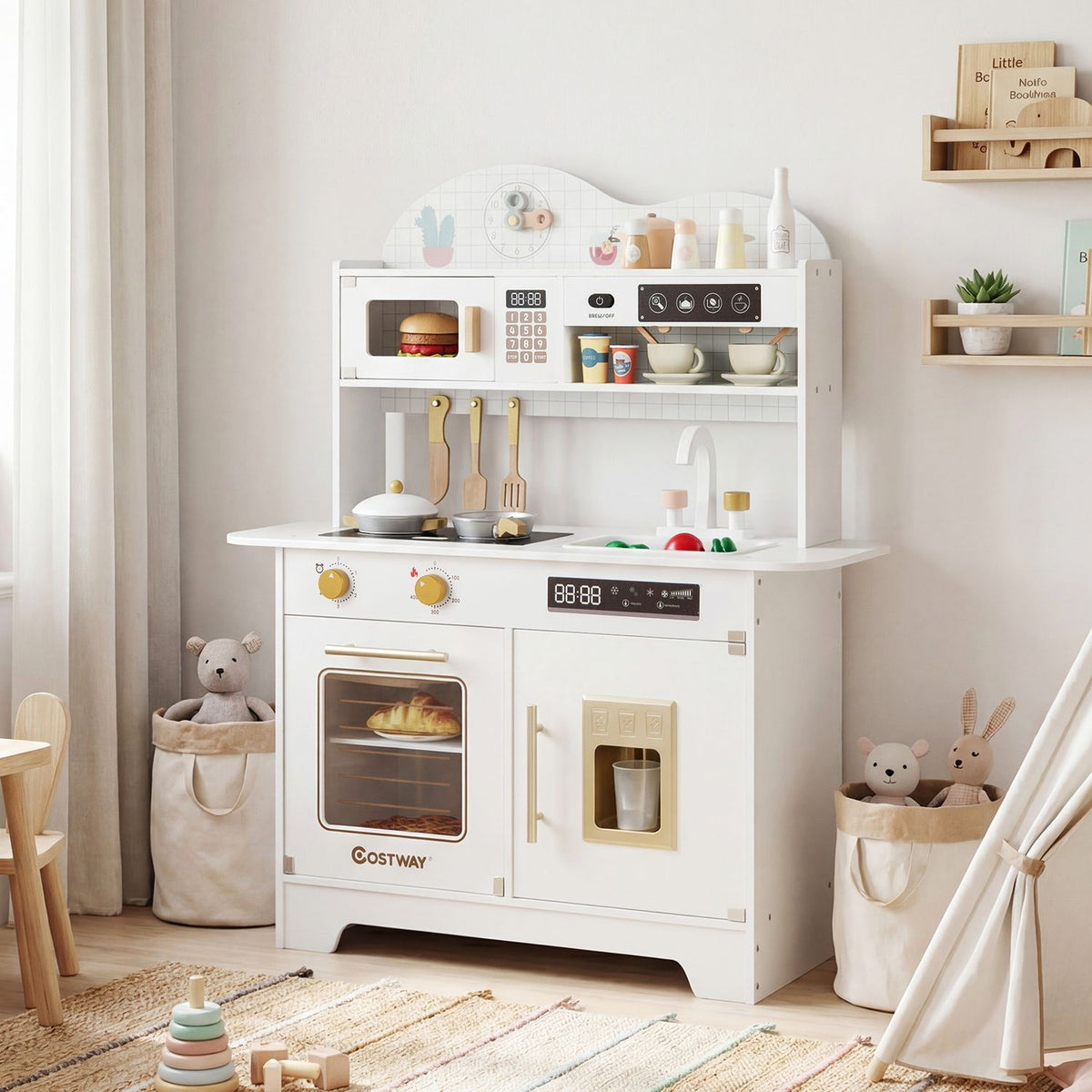 A white toy kitchen stands in a bright playroom, styled with toy dishes, pots and small decor.