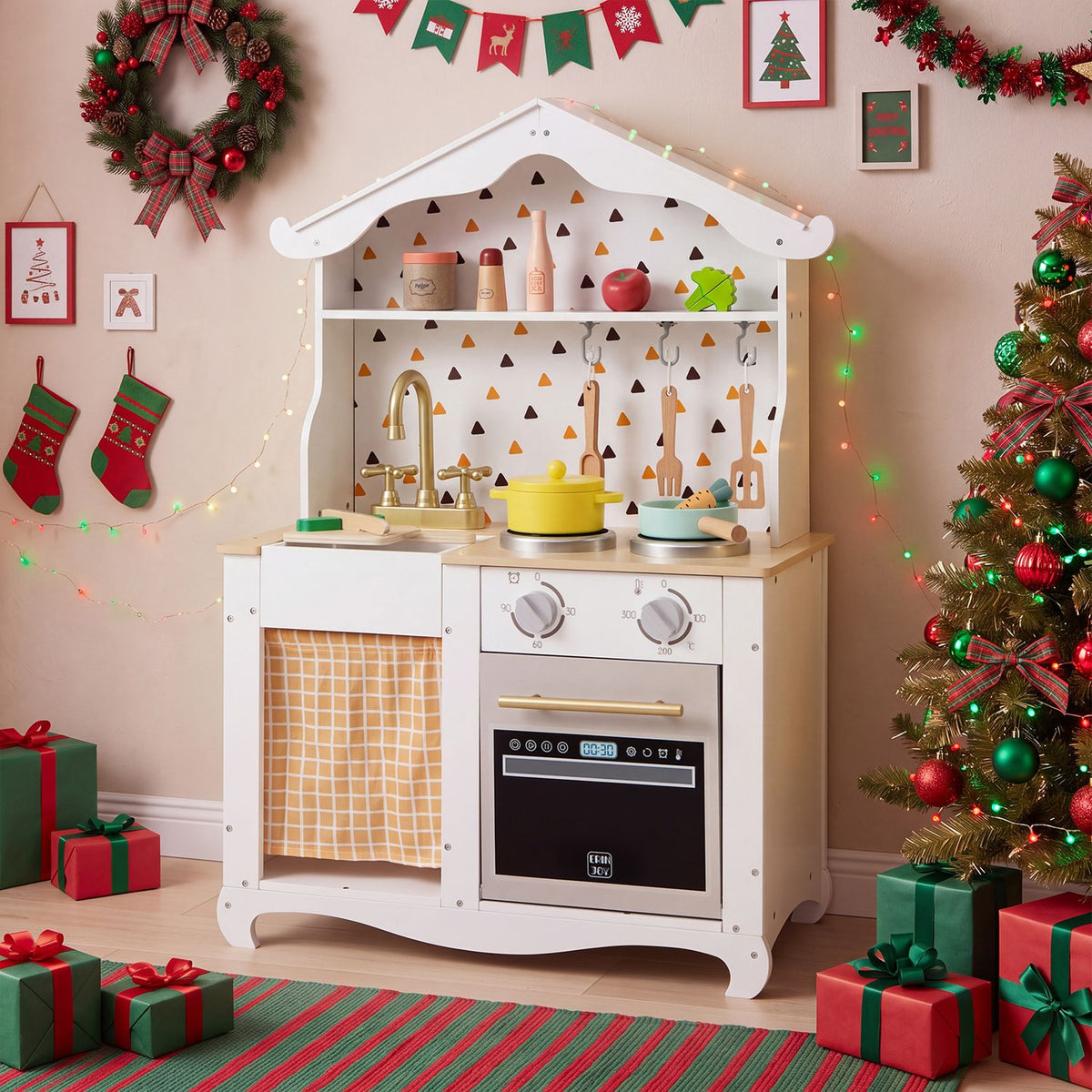White play kitchen decorated with festive lights, stockings, a wreath, presents, and a Christmas tree.