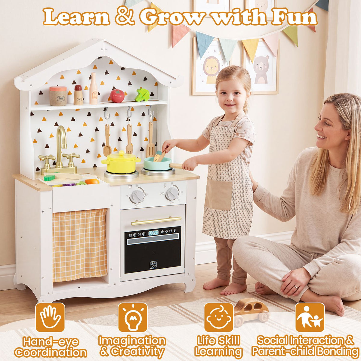 A child plays at the white toy kitchen while an adult sits beside her in a bright room.