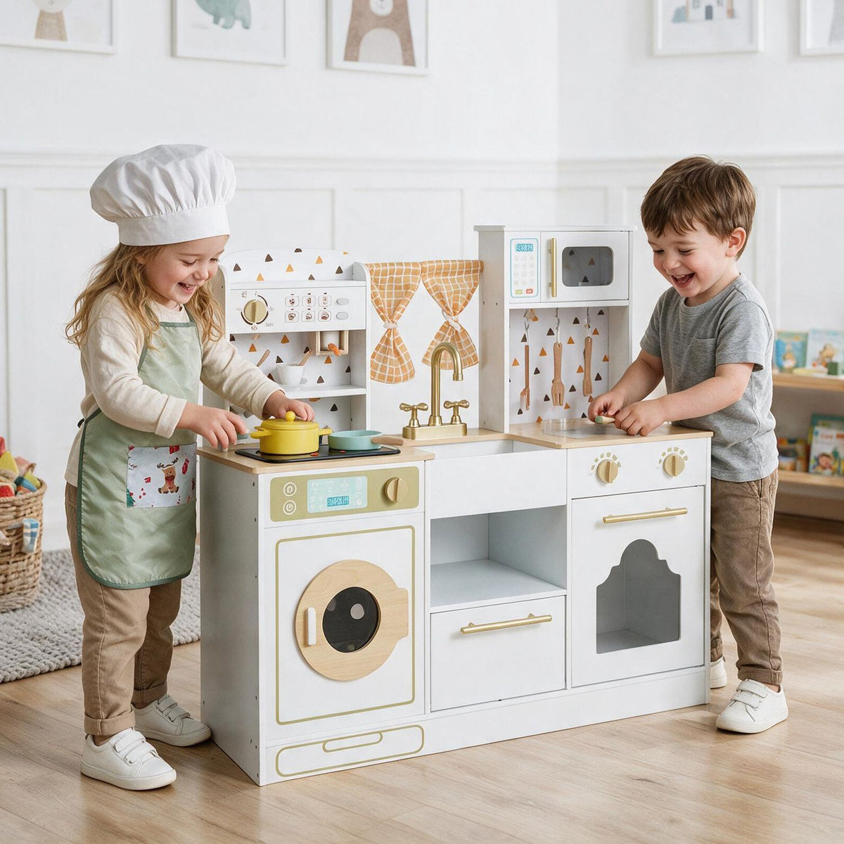 A child in a chef hat and a boy play together at a white toy kitchen with gold details.