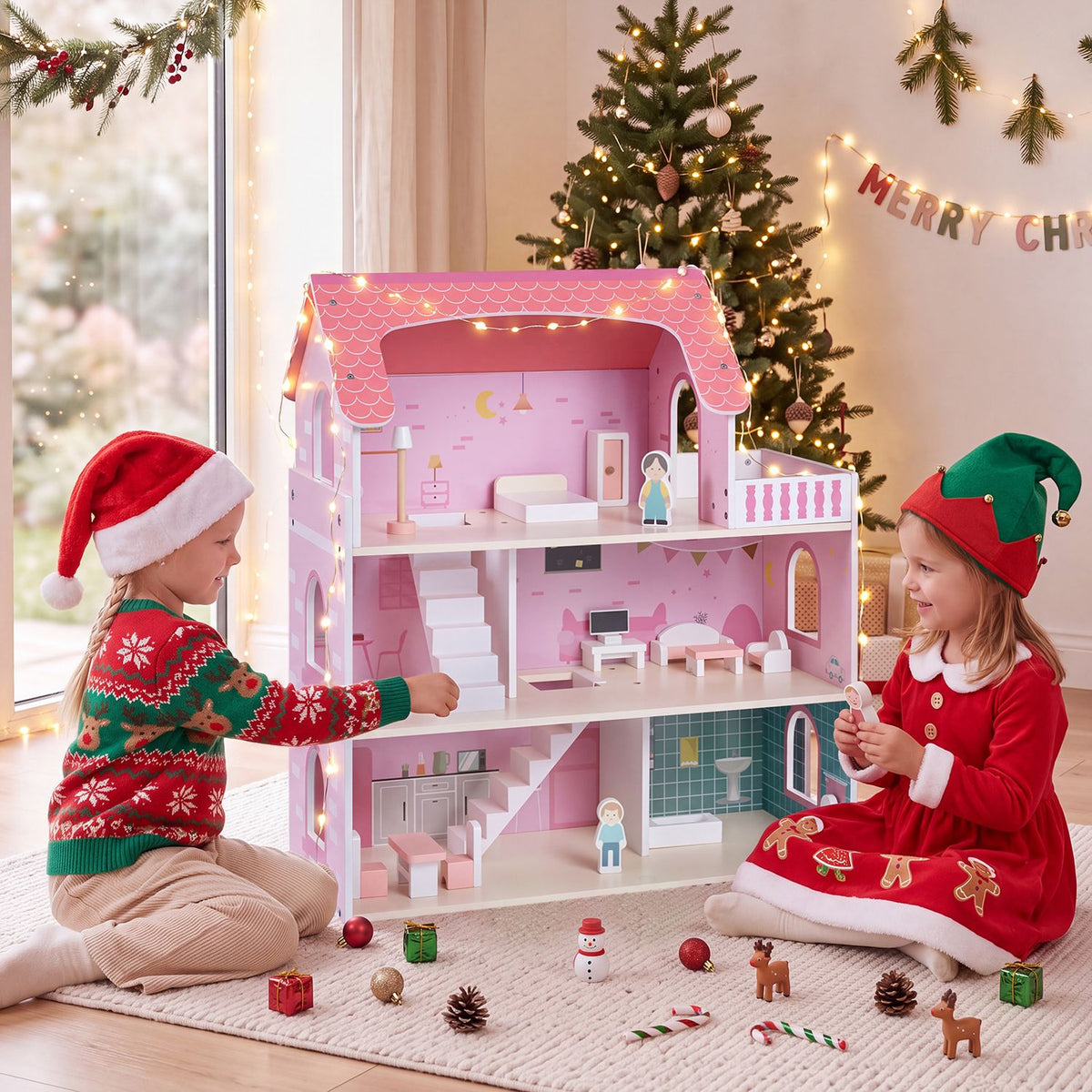 Two children play with the open pink dollhouse beside a decorated Christmas tree.