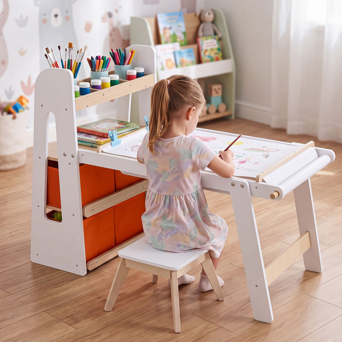 A child draws at the table, with paper rolls, art supplies, orange bins, and a stool visible.