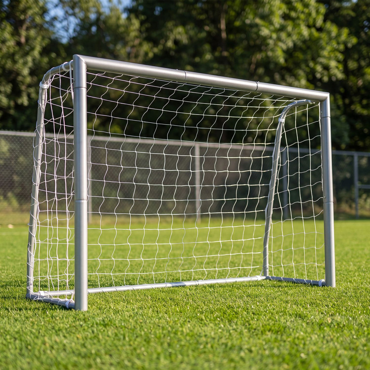 Metal soccer goal with a white net standing on a sunlit grassy field.