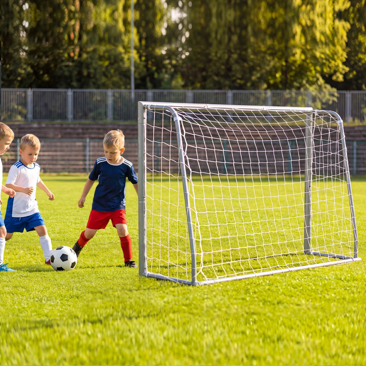 Children playing soccer beside a netted metal goal on a green field.
