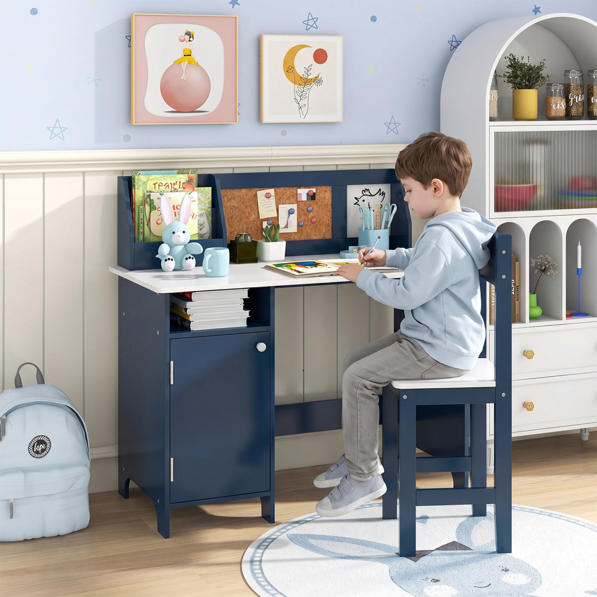 Child seated at the navy desk, drawing beside its storage cabinet and book display.