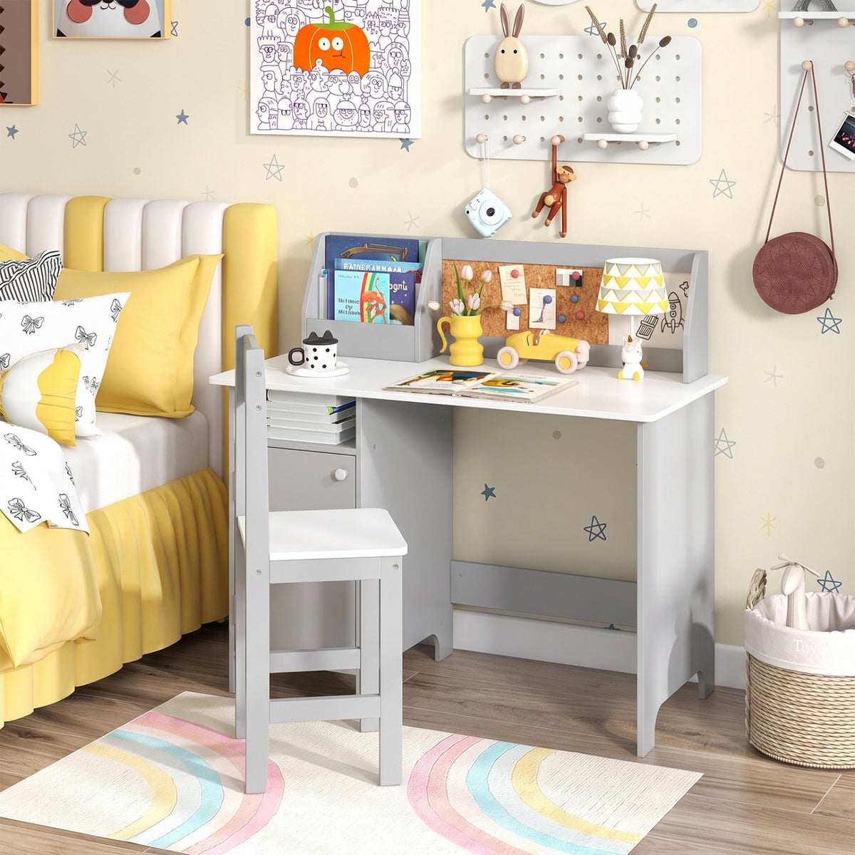 Gray children’s desk and chair beside a bed, with books and art supplies arranged on the desktop.